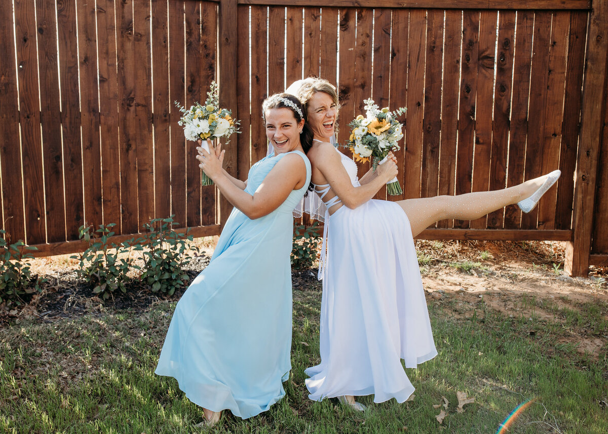 Two bridesmaids in blue and white dresses striking a playful pose with bouquets