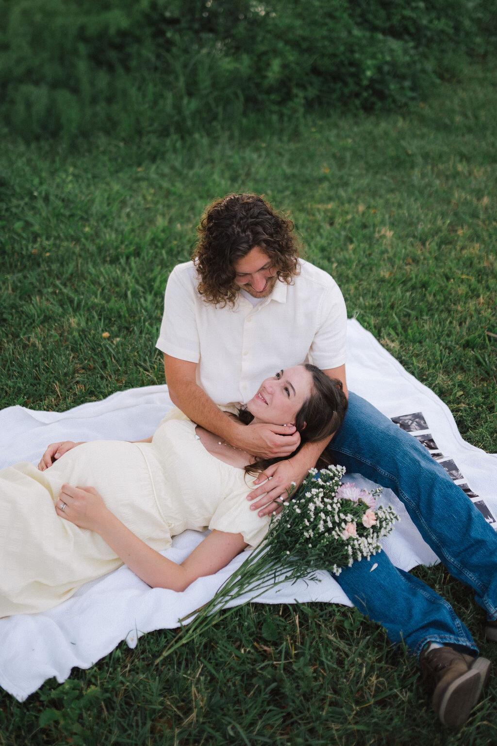 pregnant woman lies in husbands lap next to flowers in knoxville tennessee in cove lake park