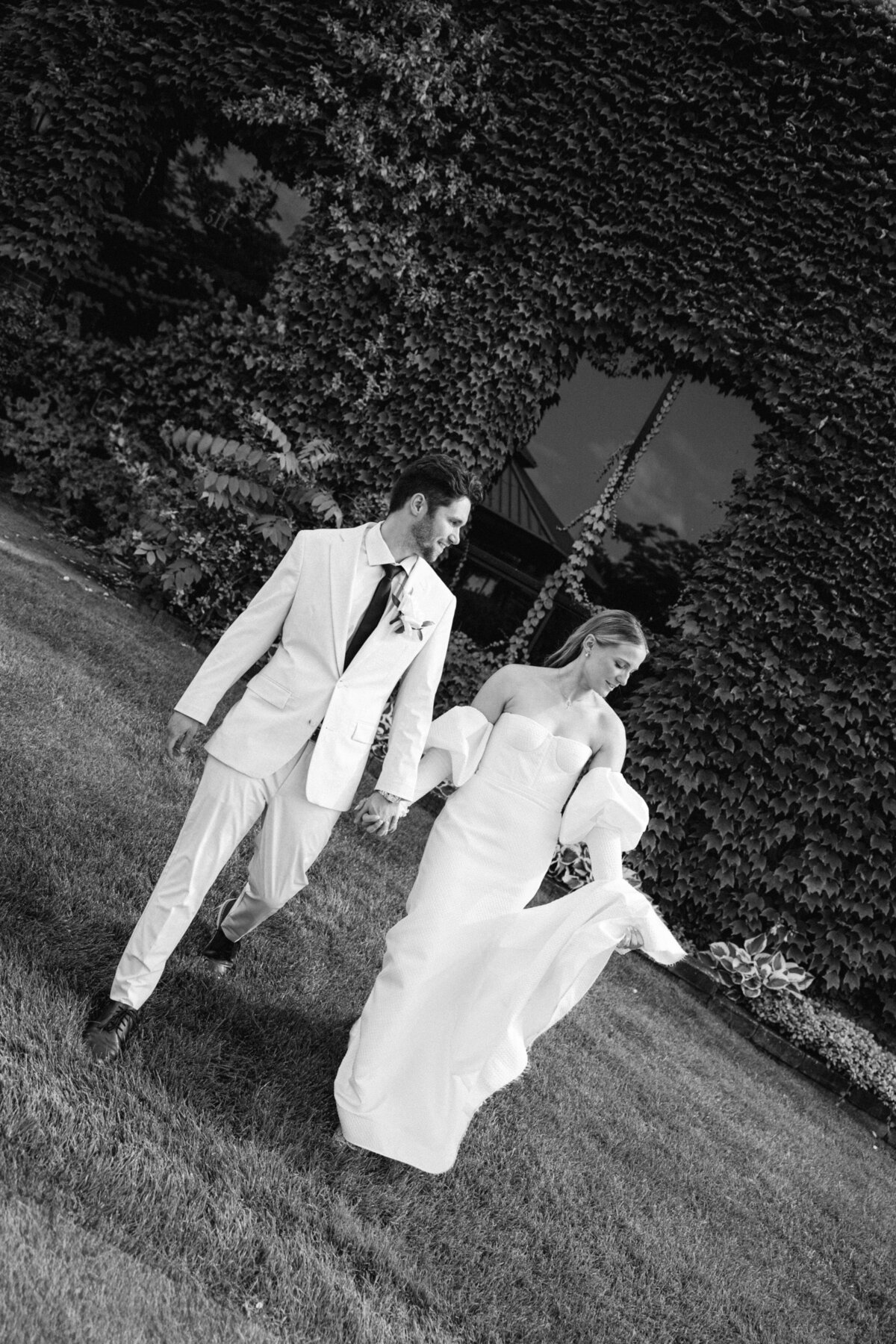 Couple stands close together in grassy field, her elegant white dress complementing the natural landscape.