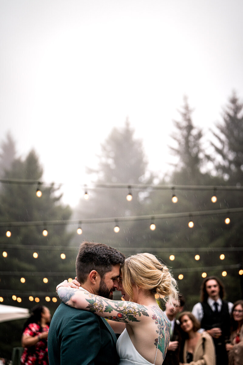 The newlywed couple shares an intimate first dance under the glowing patio lights at Ridgefield in Arcata, surrounded by fog-kissed redwoods. This magical moment captures the essence of their love story, creating timeless wedding memories in the heart of Northern California's serene beauty.