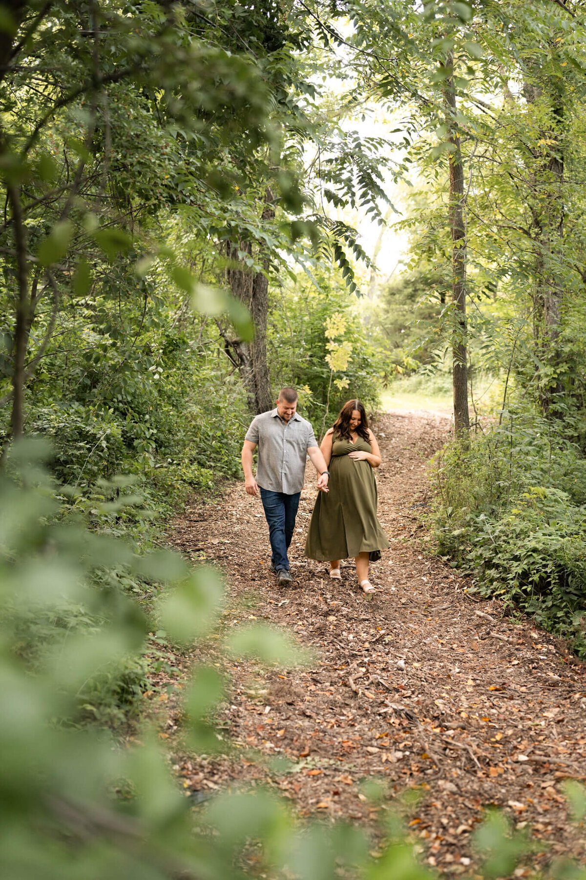 Husband and wife walking through woods while wife holds her pregnant belly