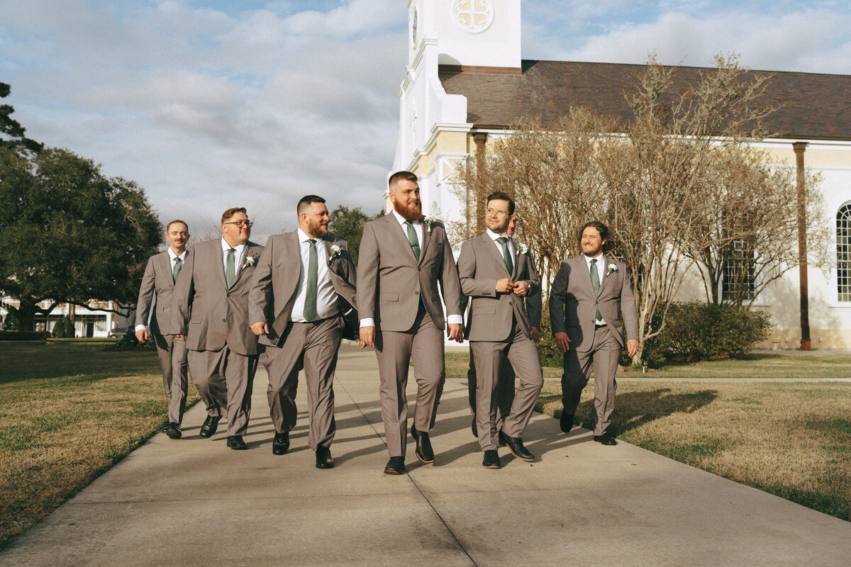 the groom and his groomsmen walking down the sidewalk in downtown st. martinville, louisiana.