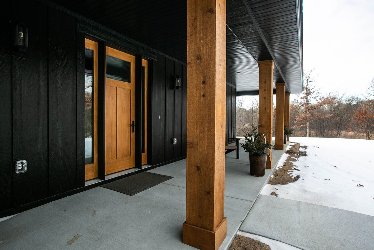 Exterior view of custom home in Elk River, Minnesota with black siding, wood details and front porch built by Cornerstone Custom Builds