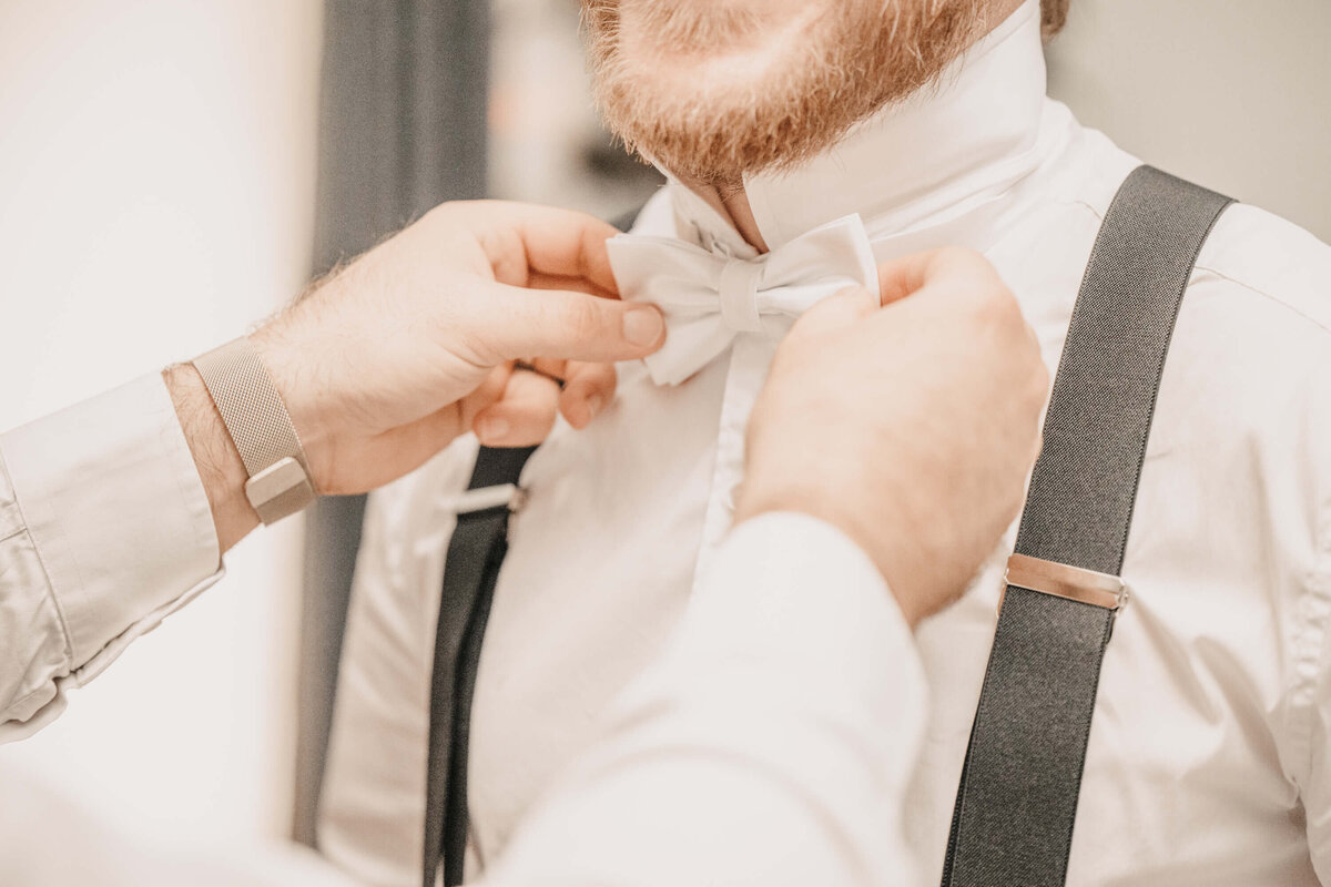 A man in formal attire is adjusting his bow tie, preparing for a special event or occasion. - photo by Jamie Simmons
