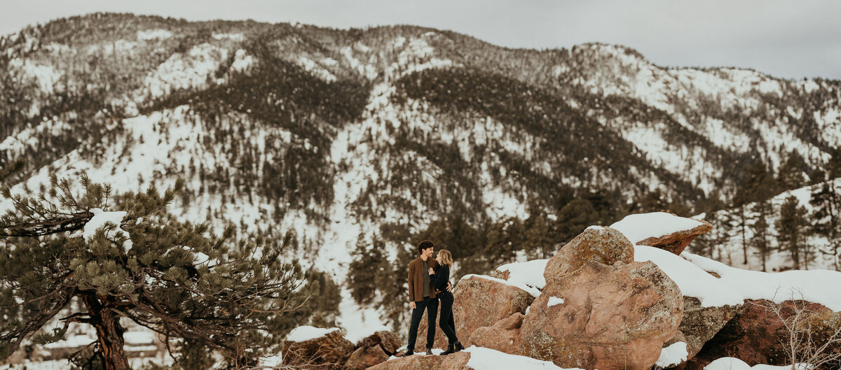 couple stands on snowy rocks