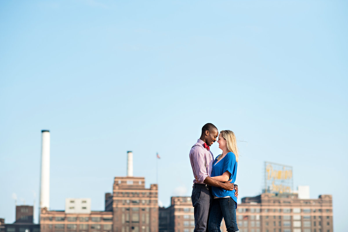 An engaged couple kiss with the Baltimore cityscape behind them.