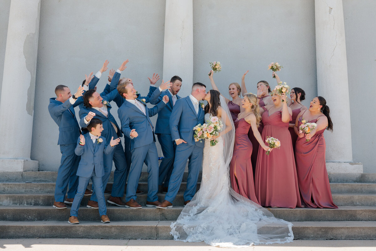 Groom helps bride carry her dress and veil as she walks up the stairs at a historic Mansion. Photo by Anna Brace, who specializes in Kansas City Wedding Photography.