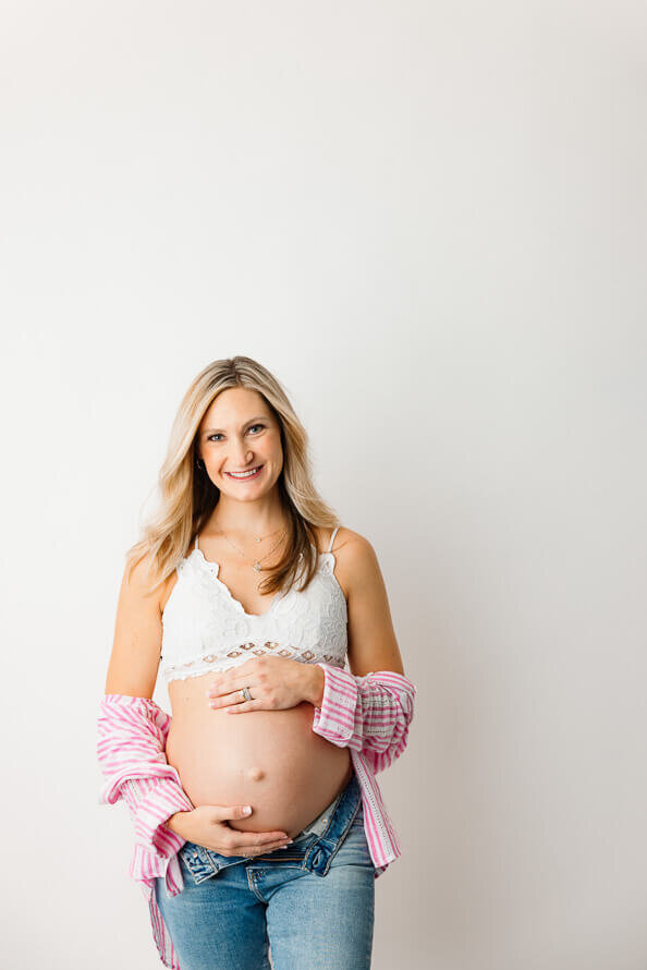 A mom poses for the camera while holding her pregnant belly.