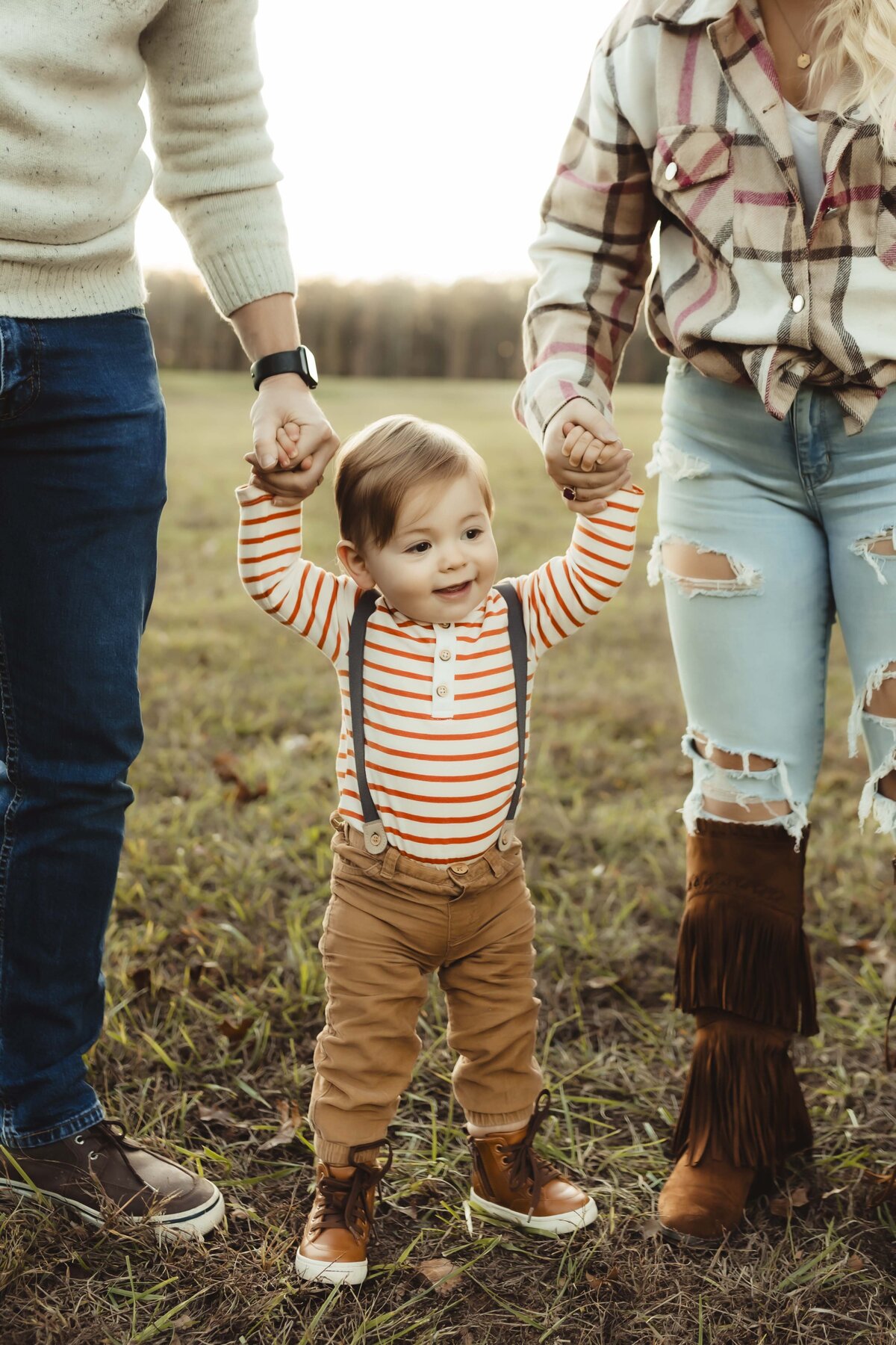 Toddler boy holding mother and fathers hand during golden hour on a fall Missouri day