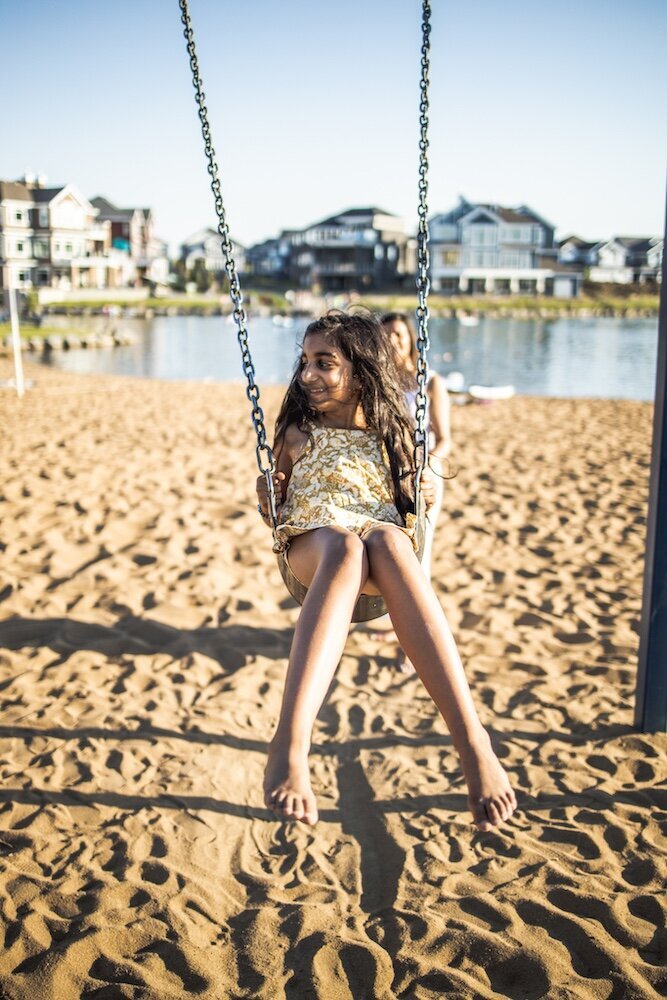 Mom in a white dress pushing her son and daughter on a swing 