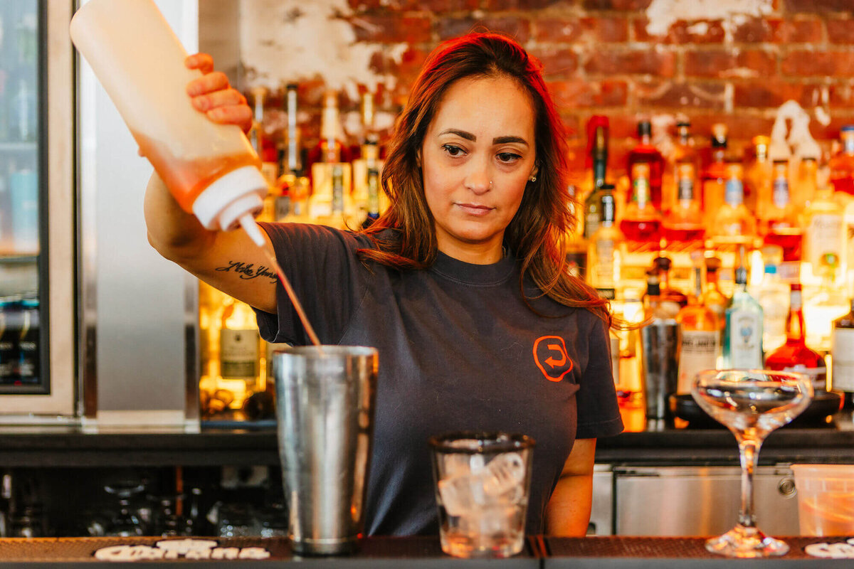 drifter's bar tender pouring a red colored mixer into a cocktail shaker
