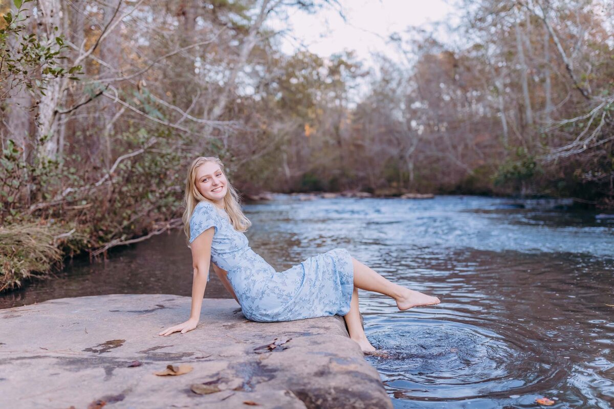 A senior portrait of a girl sitting on a rock kicking her feet in the water of Line Creek in Peachtree City, Georgia.