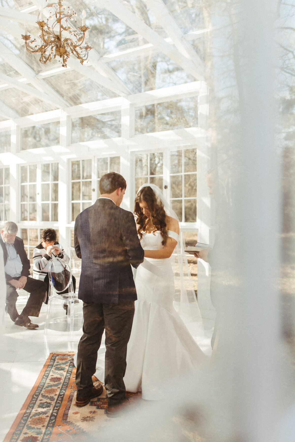 View of a bride and groom exchanging vows from the outside of the atelier through a window