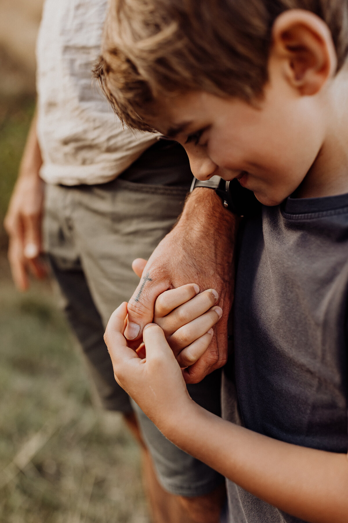 A little boy holding his dads hand and smiling while walking in a field of grass, lucy jane photography is the artist of this photo