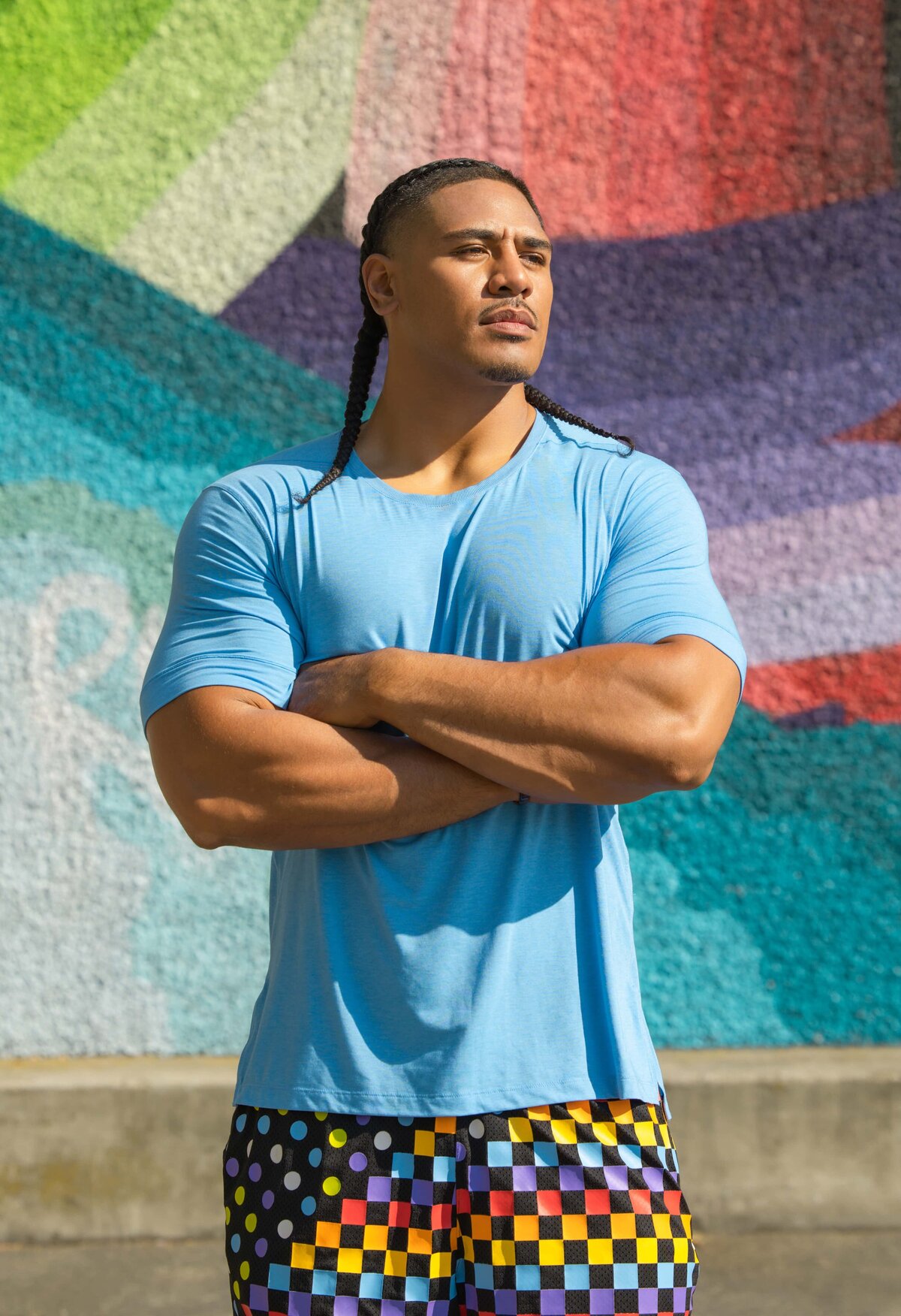 An athletic man poses in front of a colorful wall in downtown San Jose
