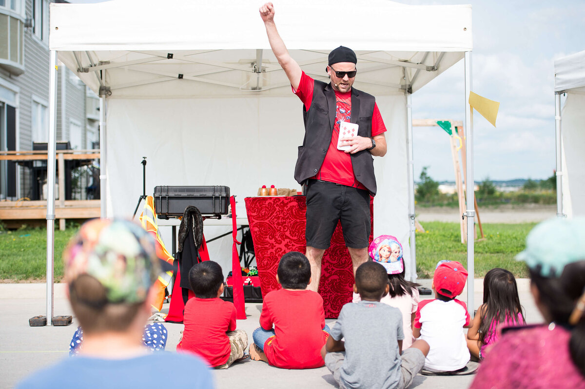 a magician in a red t-shirt doing a trick during a corporate children's event.  Captured by Ottawa Event Photographer JEMMAN Photography COMMERCIAL