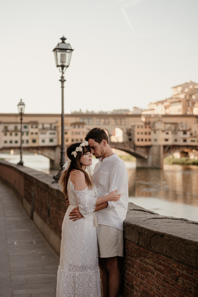 Love session au lever du soleil à Florence, en Italie, capturant un moment tendre entre un couple devant le célèbre Ponte Vecchio.