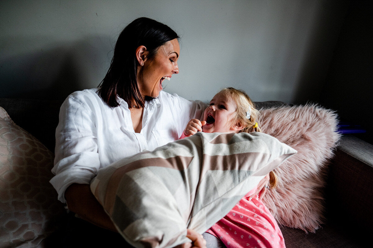Mum on the sofa laighing at her little daughter who is laughing back