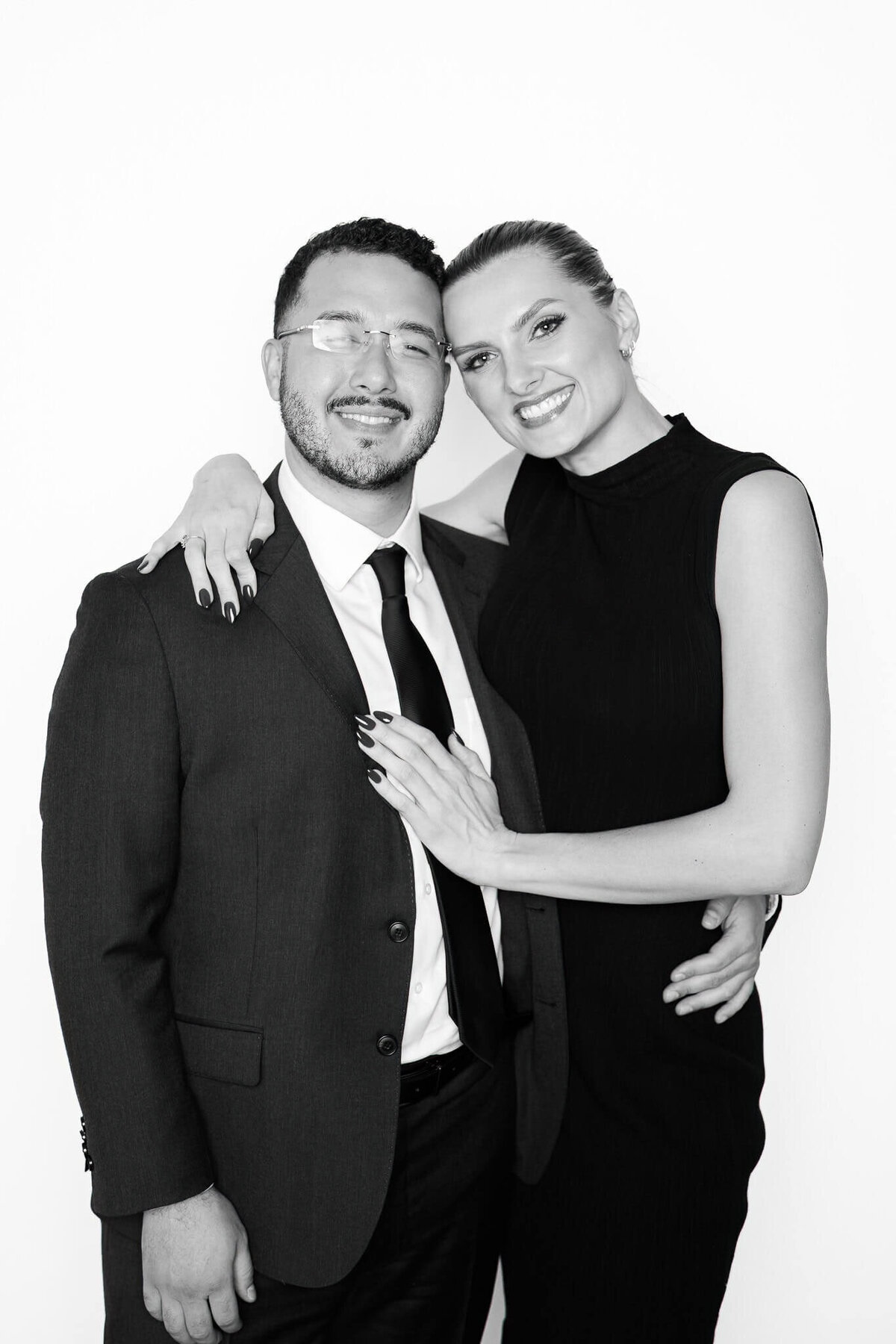 A couple dressed in formal black attire smiling for a black and white portrait taken by Monochrome Portraits, a modern Phoenix photo booth experience.