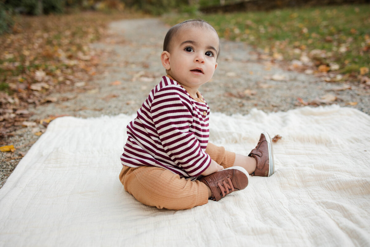baby boy sitting on a blanket outside smiling in the fall