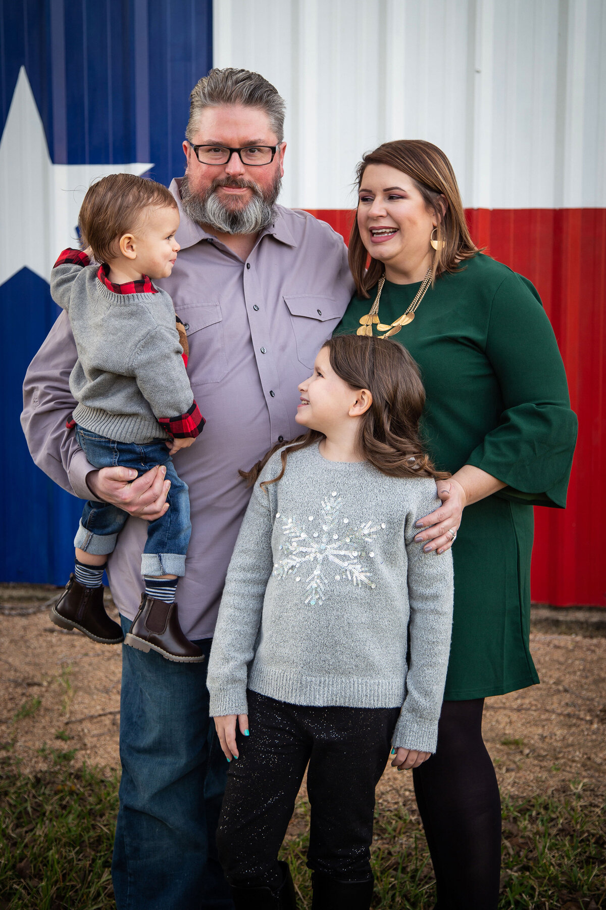 family of 4 snuggling in front of a barn with the TX flag painted on it
