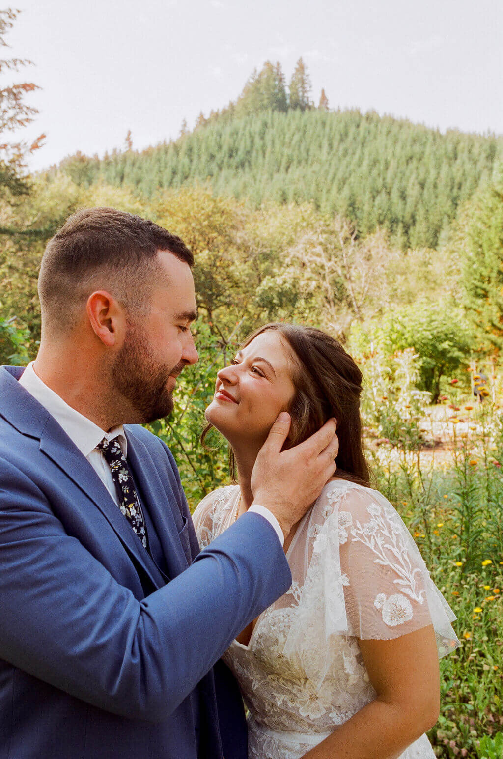 A bride and groom smile at each other while the groom places his hand on her face.