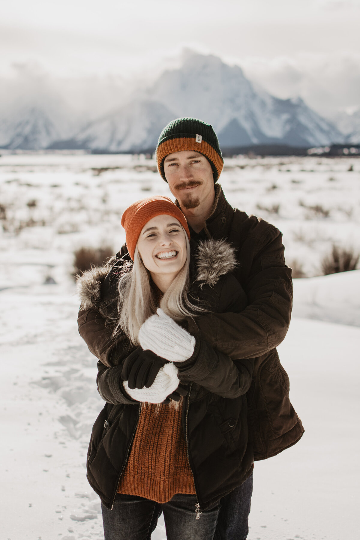 man holding his fiance around the shoulder as they smile for their winter engagement in Jackson Hole Wyoming