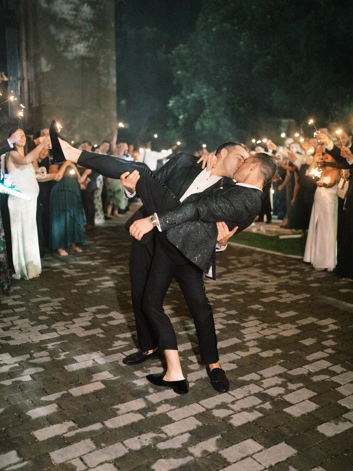 A romantic dip kiss shared between a couple amidst celebration, highlighting love and connection during a joyful nighttime gathering with loved ones.