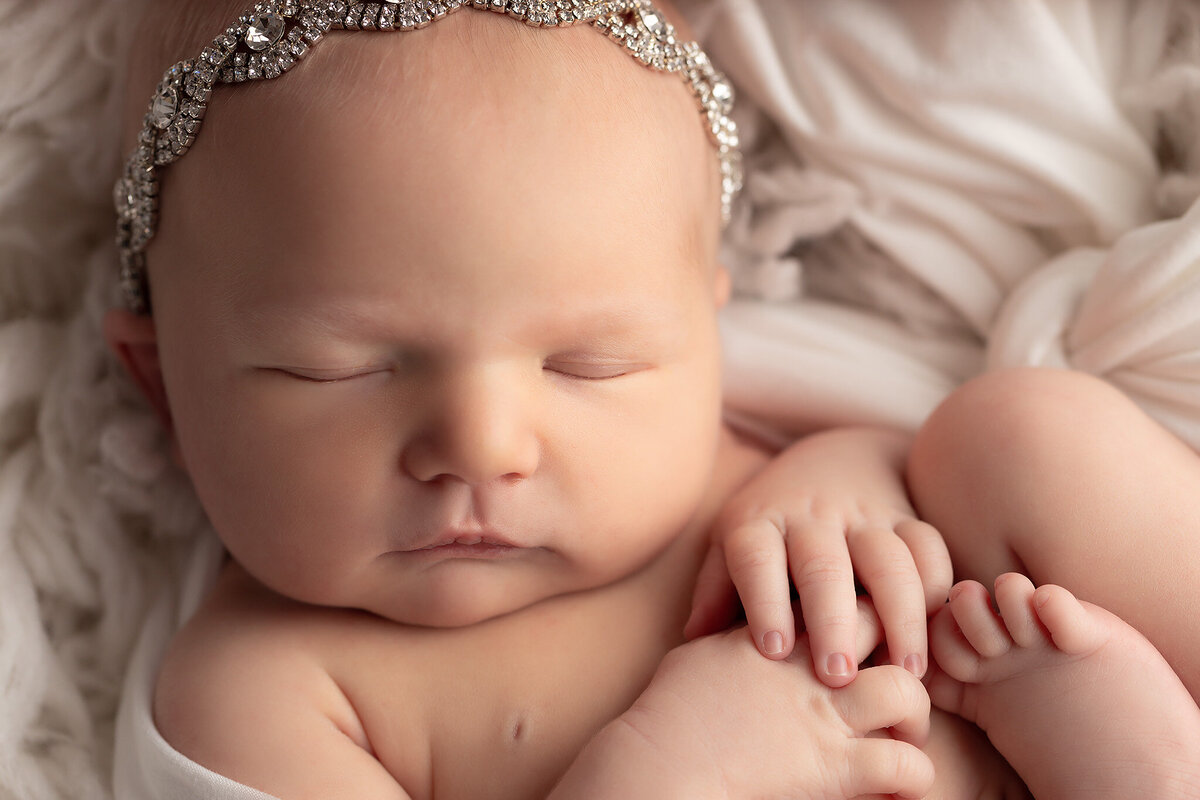 Baby girl wrapped in white with a sparkling crystal headband, showcasing newborn photography studio style for elegant newborn pictures and classic baby photography.