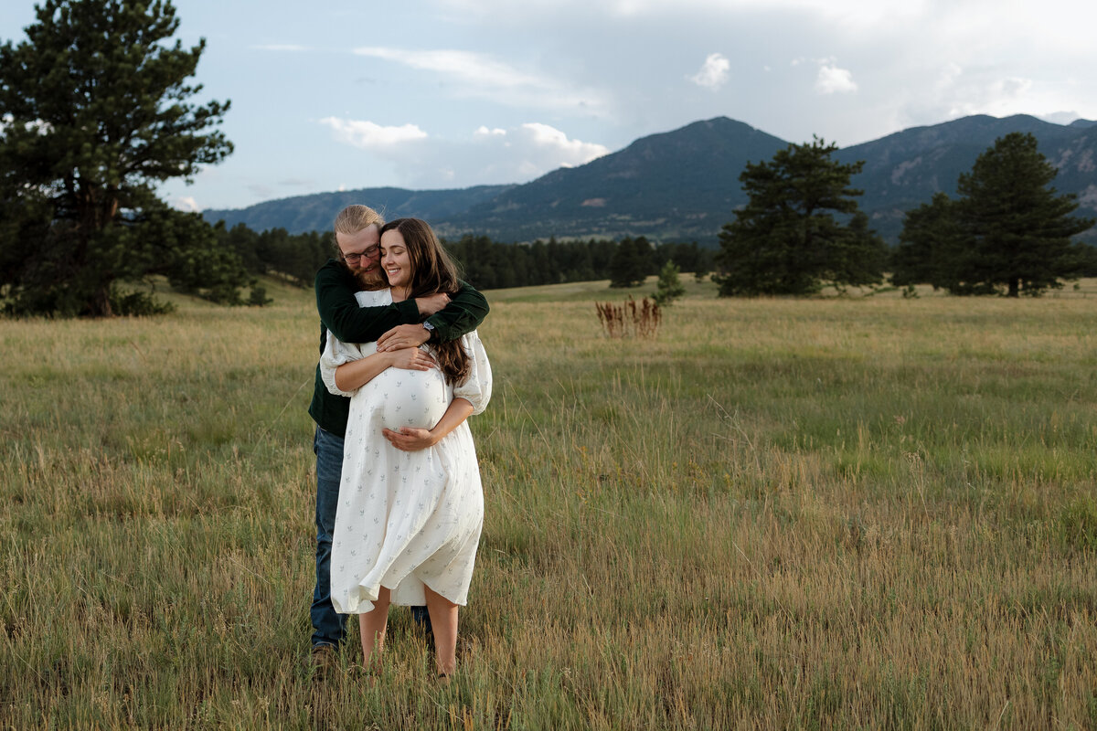 Expectant parents in Firestone Colorado hugging each other with mountains in the background