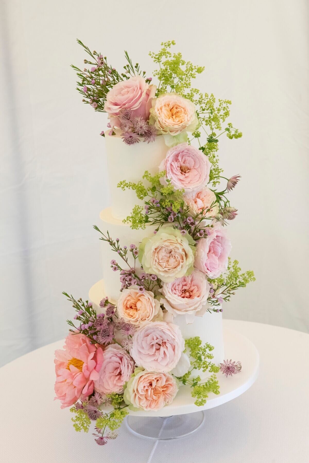 Pale wedding cake with 3 tiers and heavy florals running down the length of the cake