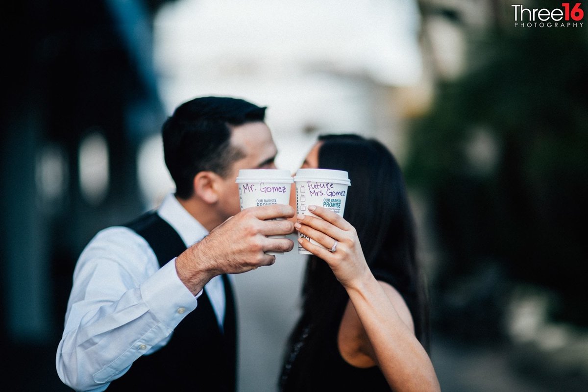 Engaged couple share a kiss hidden behind two Starbucks coffee cups