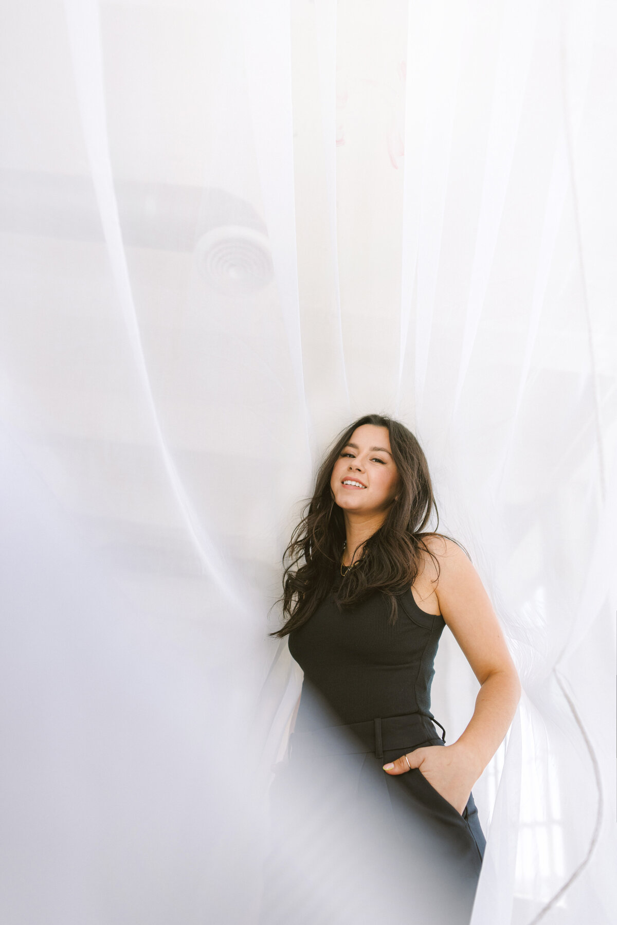 Modern branding photo of a woman in a black outfit standing confidently behind sheer white curtains. Captured in Greenville SC by Dani Lacey.
