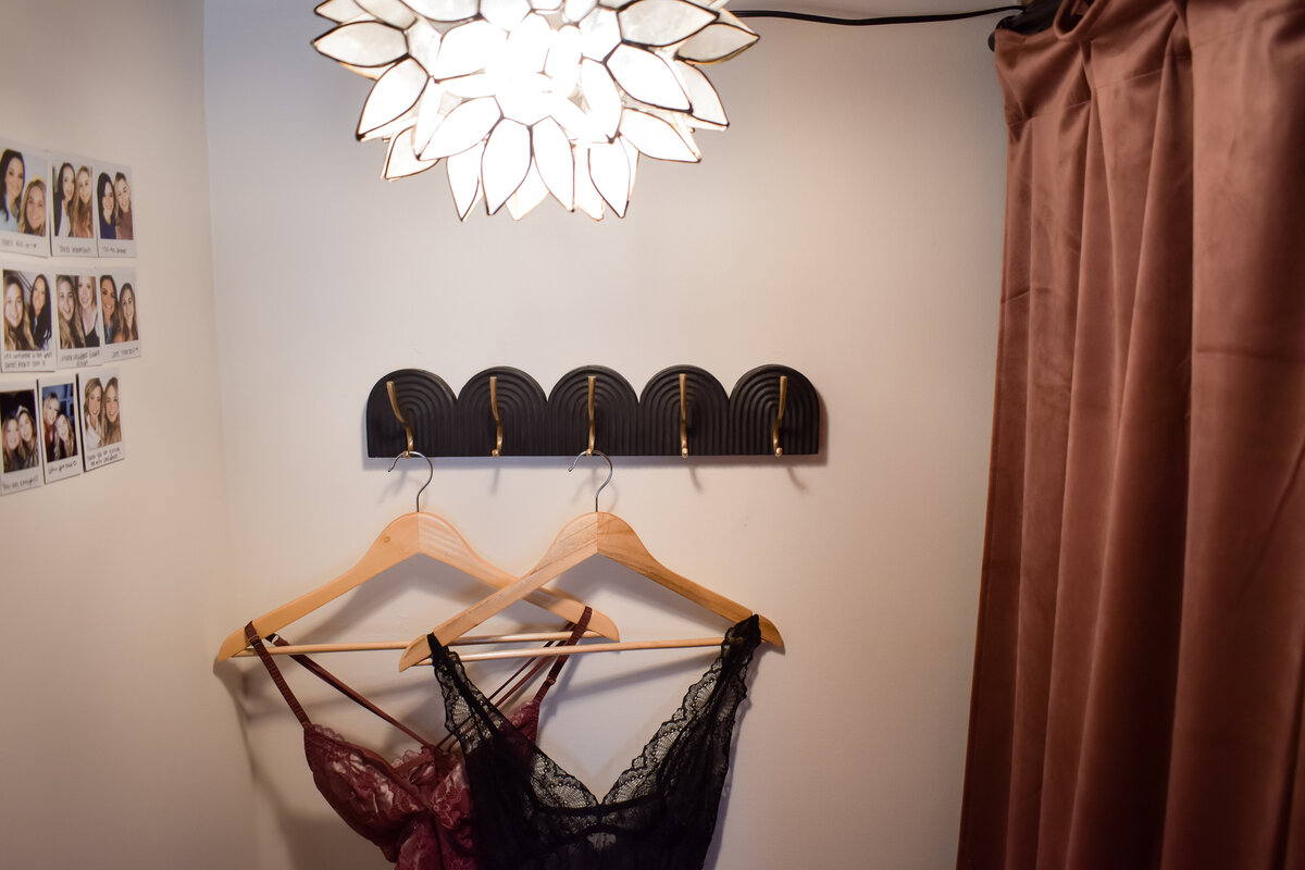Two dresses hang in a small dressing room with textured curtains