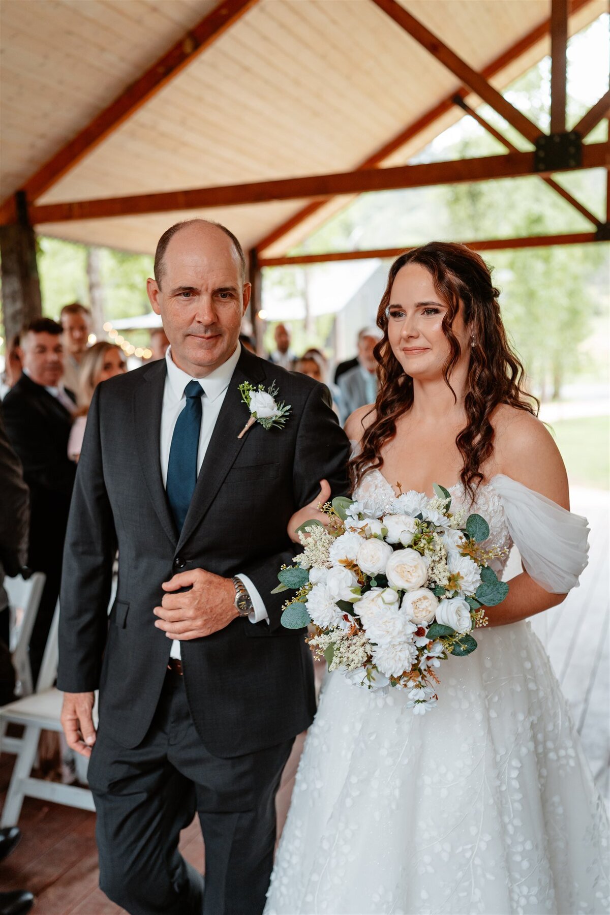 A radiant bride, her hand gently clasped in her father's, glides down the aisle, her eyes gleaming with anticipation and joy.
