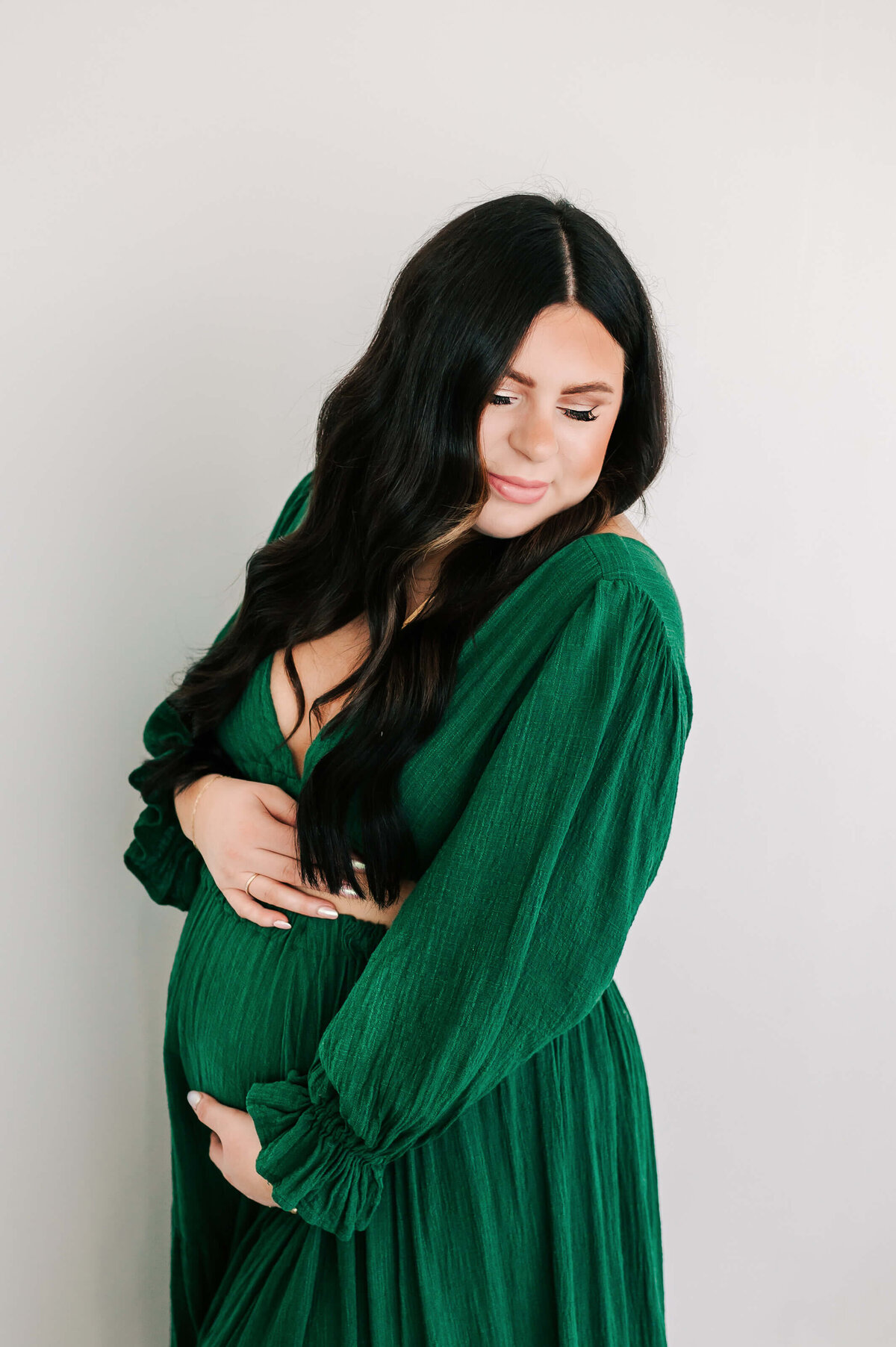 matenrity pictures of pregnant mom in green dress hugging baby bump