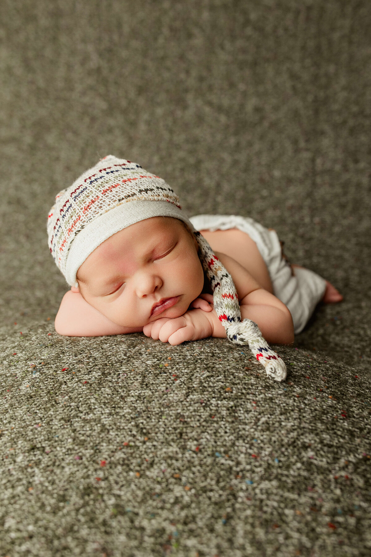 newborn baby boy in a multicolored sleep cap posed sleeping on a green sweater knit background
