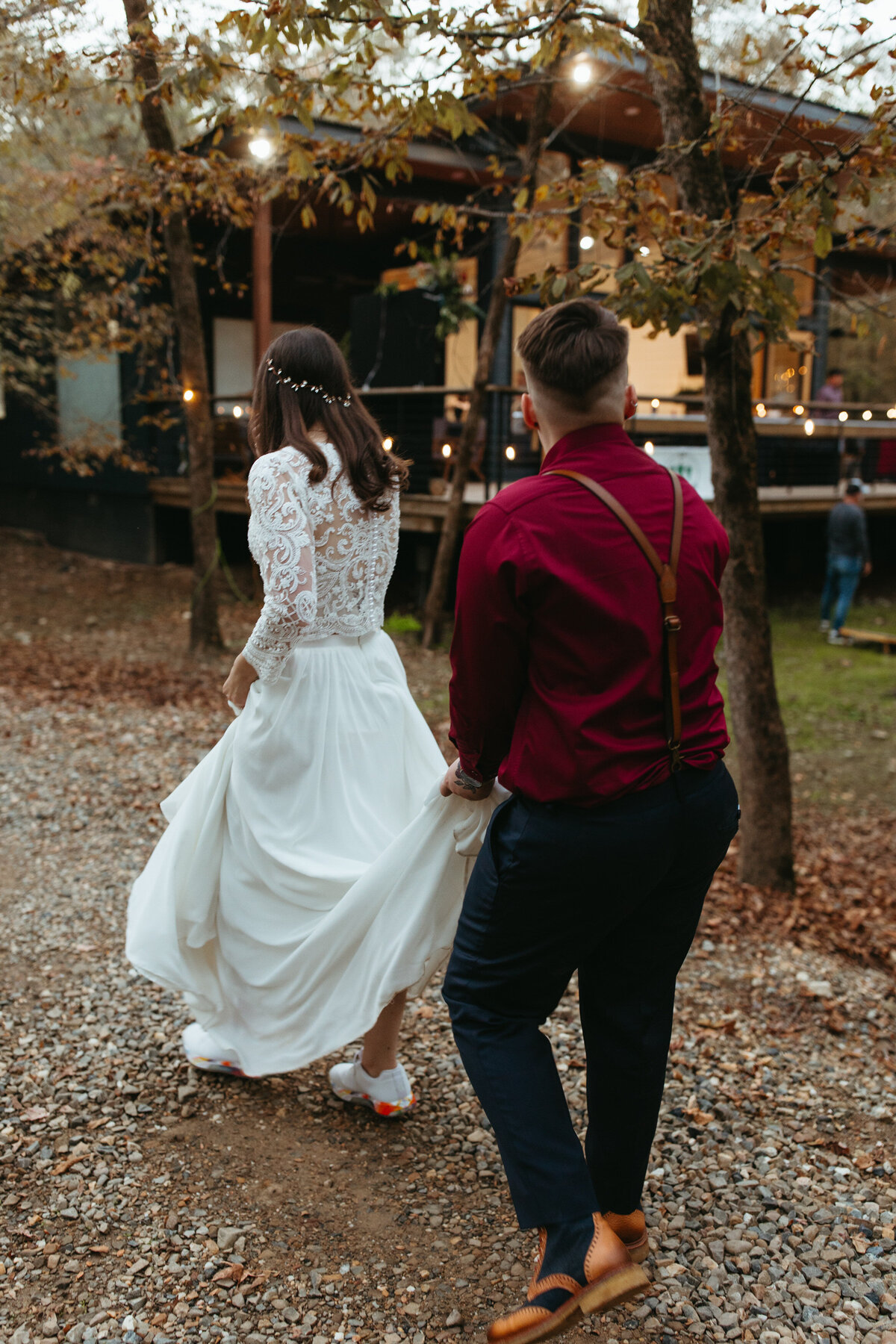 Wedding couple walking along a path as one holds the back of the other's dress up.