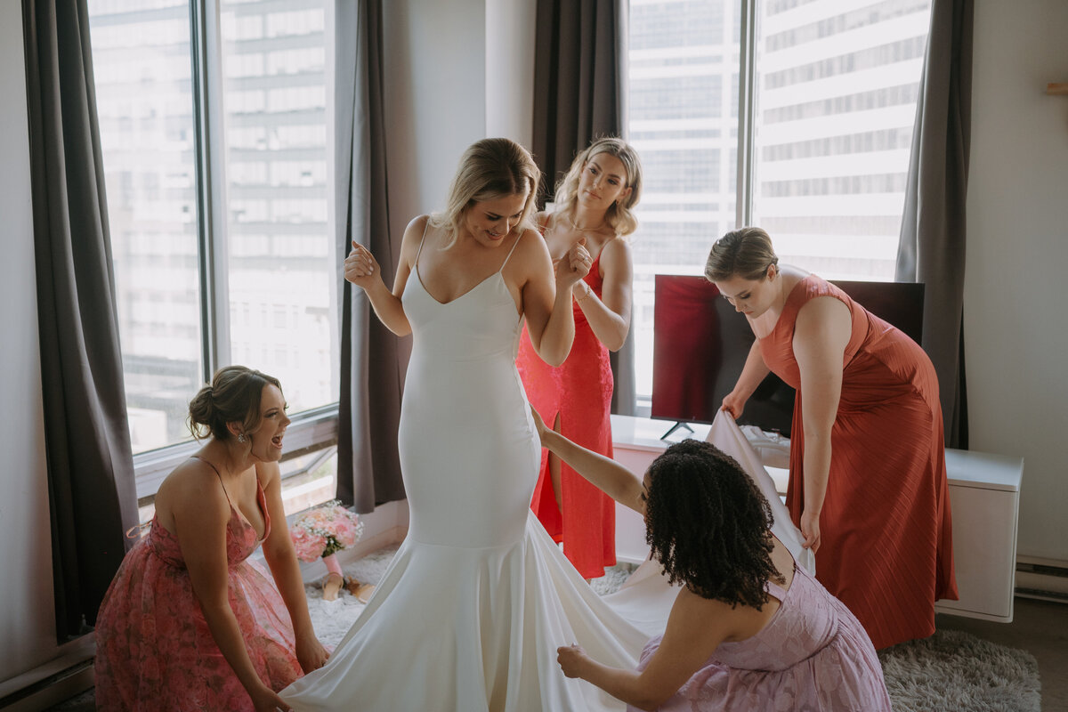 bridesmaids helping bride into weddig dress