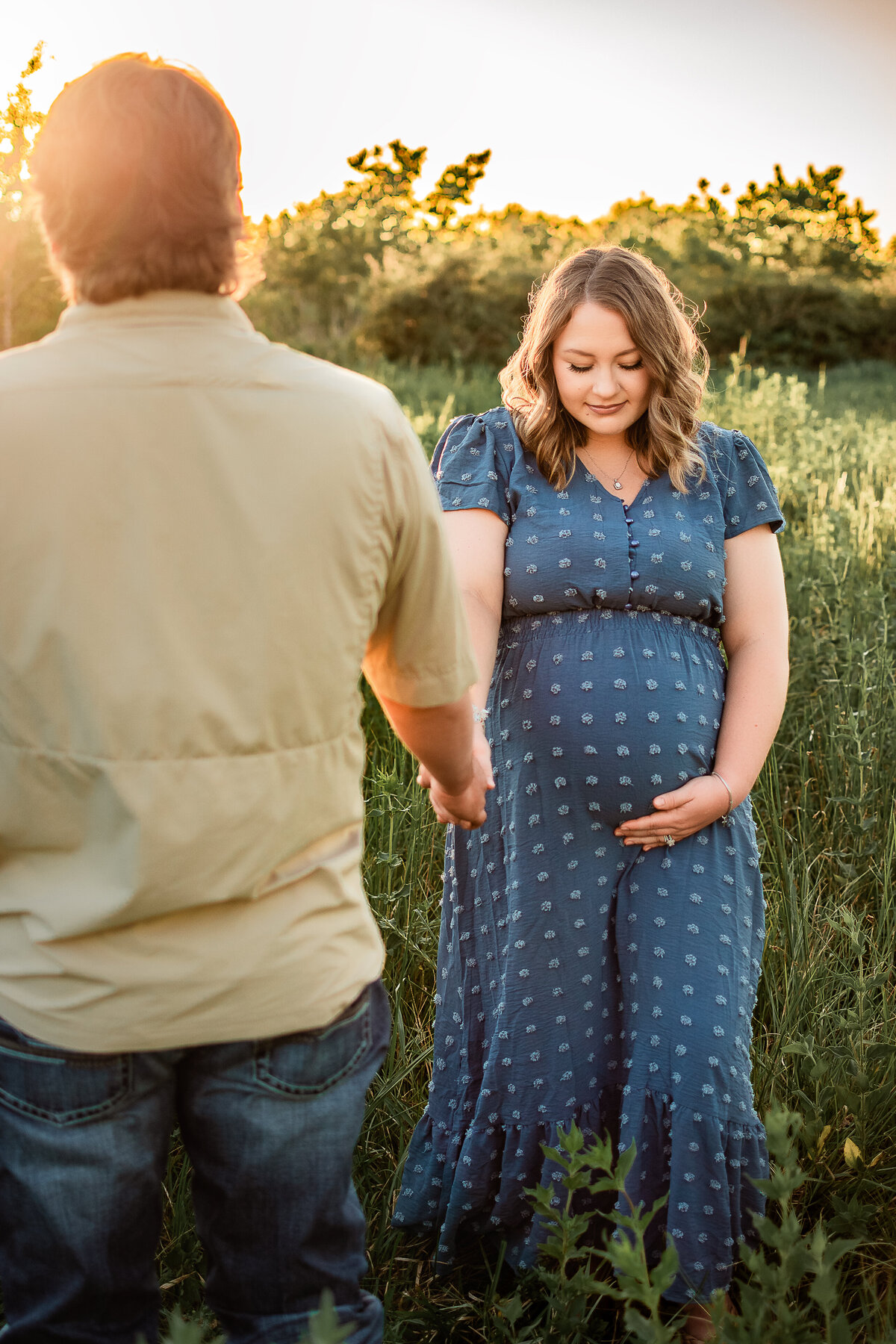 A mom to be looks down at her belly while she holds her husband's hand.