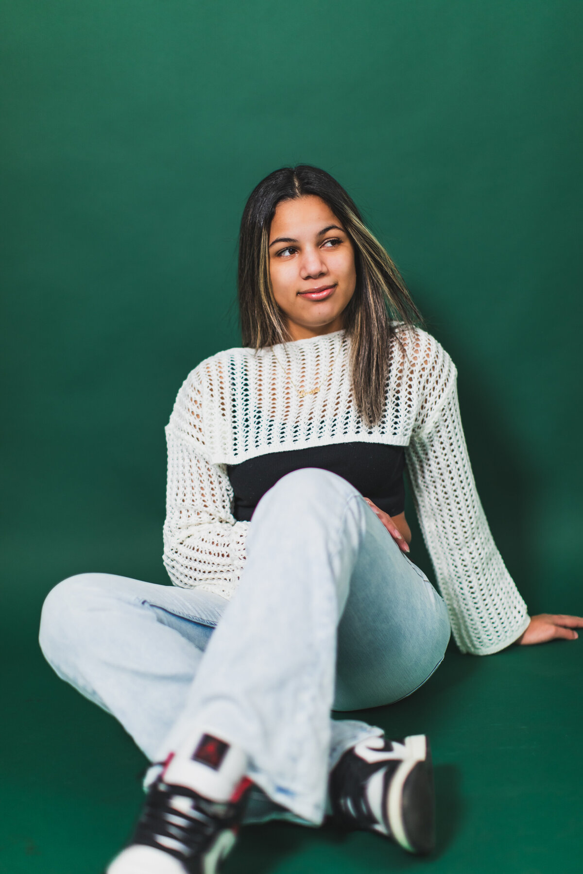 this hispanic girl smirks and looks on as her hair is blown by a fan at the Pittsburgh Photography Studio during her senior photo shoot.
