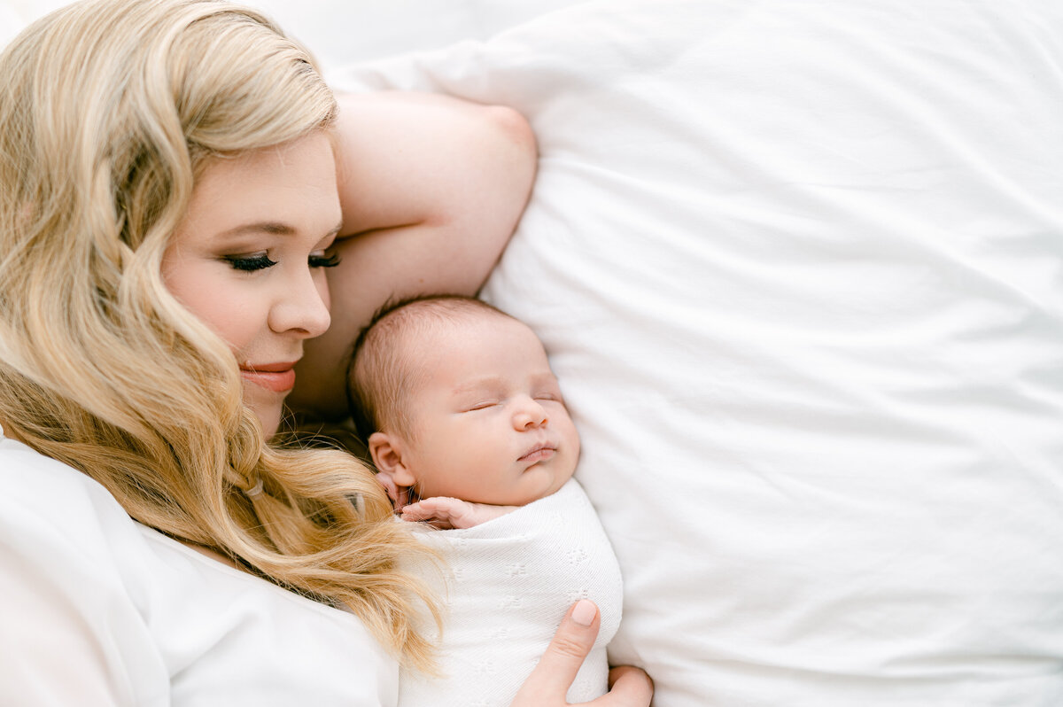 Mom lays on her left side next to her baby on a bed