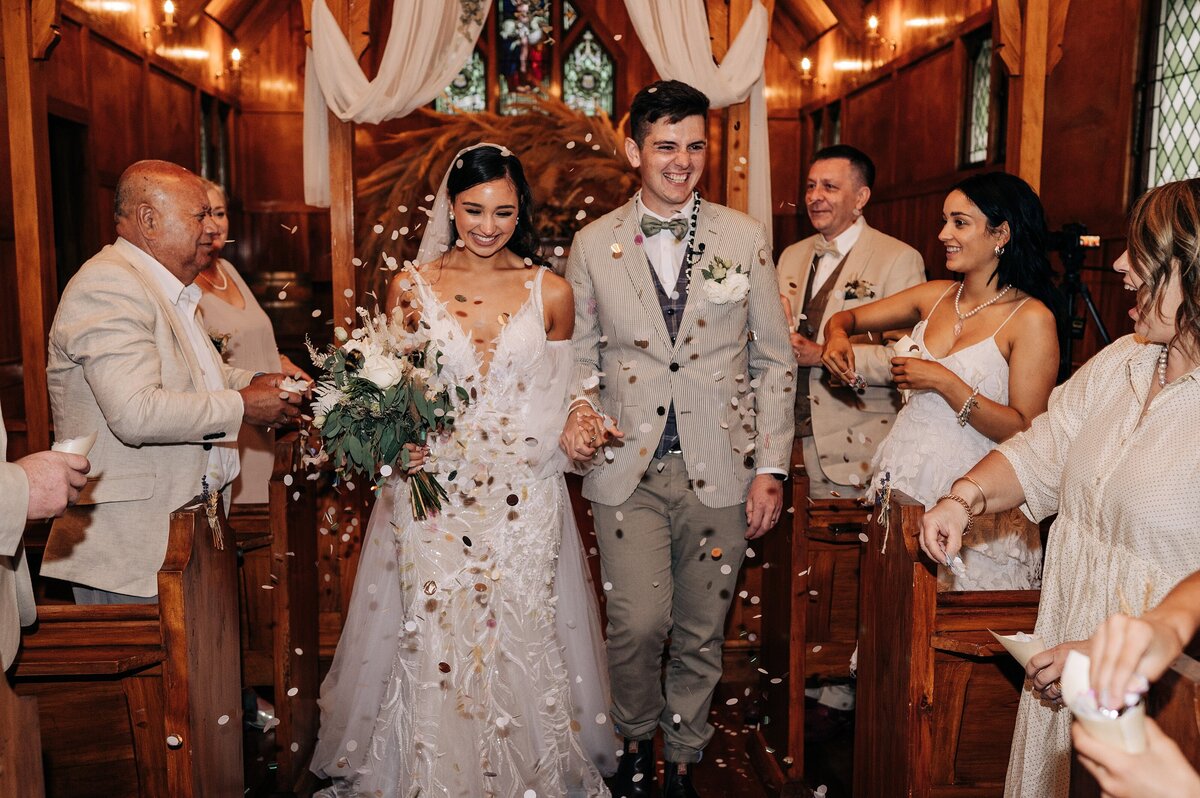 bride and groom walk down church aisle while guests throw whole bride silver and white confetti at the farm chapel near gore