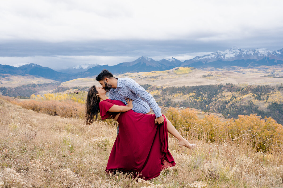 Couple dips in a kiss on the mountain side in Telluride, Colorado. Bride wears a flowing red dress