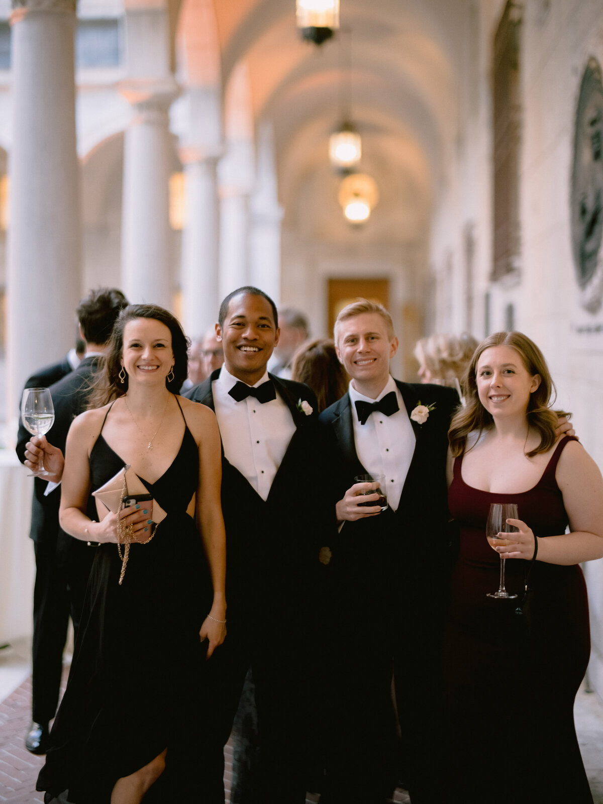 Wedding guests pose with drinks in the courtyard of a Boston Public Library wedding cocktail hour