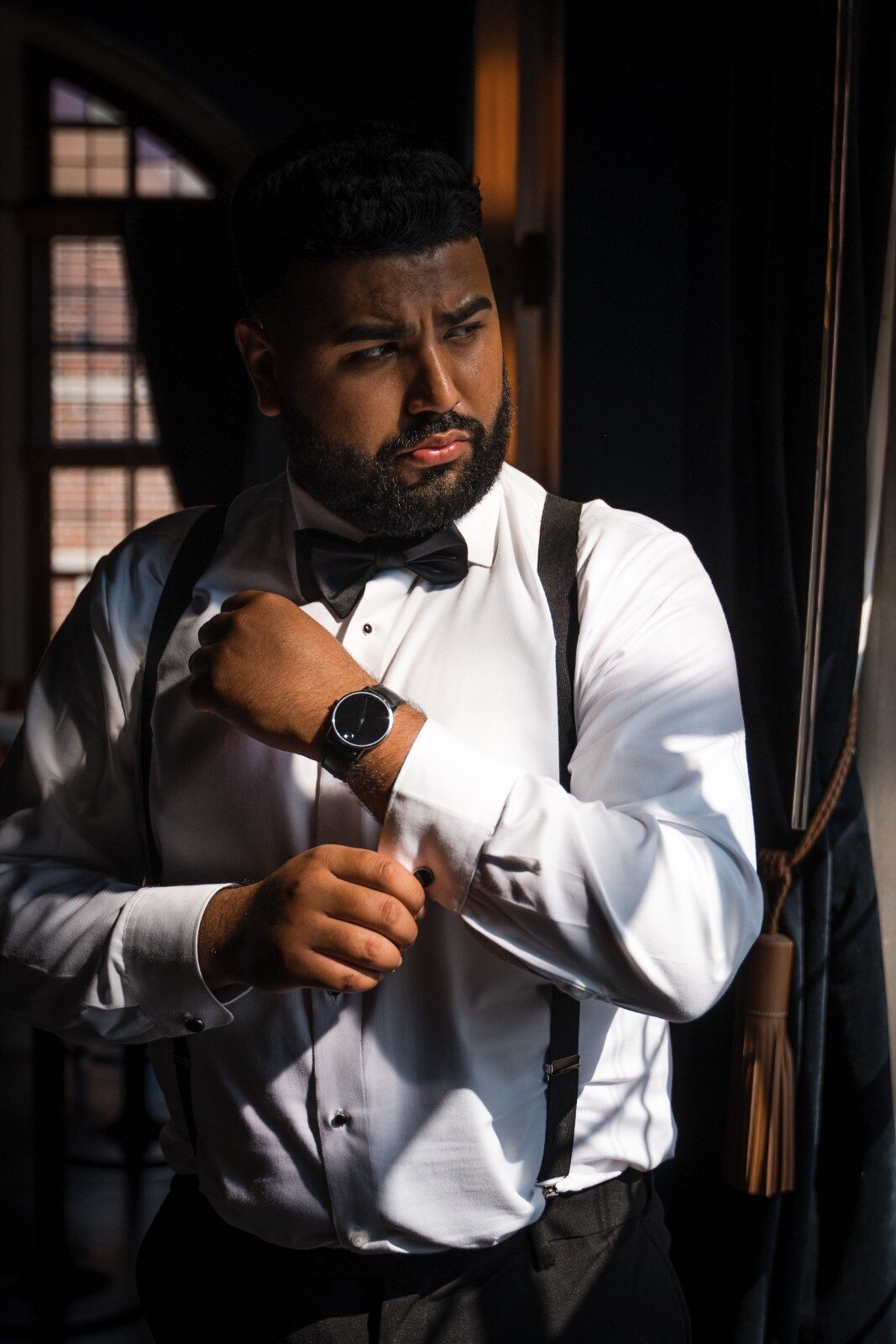 Groom adjusting cufflinks in moody window light at Union Club Hotel.