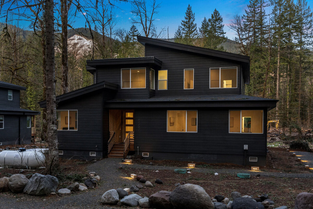 Modern black cabin exterior surrounded by a forest at dusk