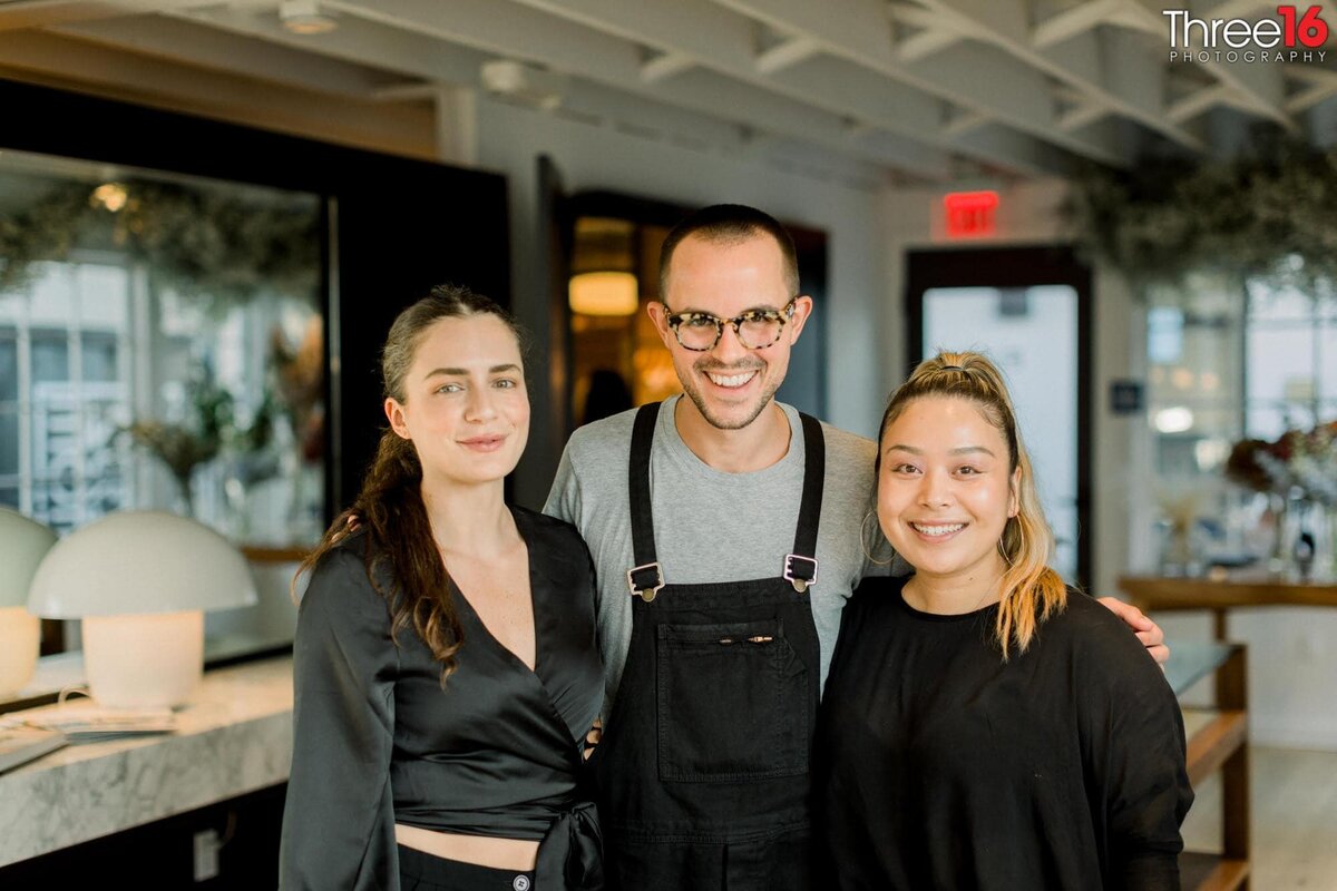 Three employees pose together during a grand opening for their shop
