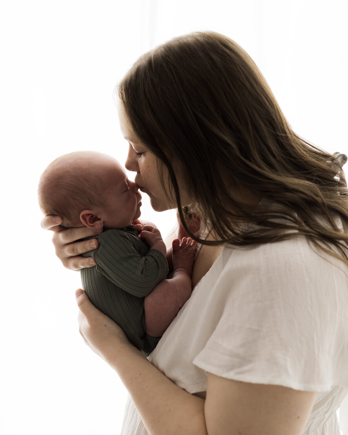mom in white dress holding newborn baby boy in green onesie