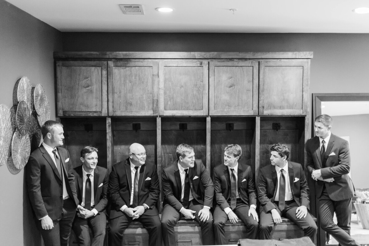 A groom and his groomsmen sit in wooden lockers chatting
